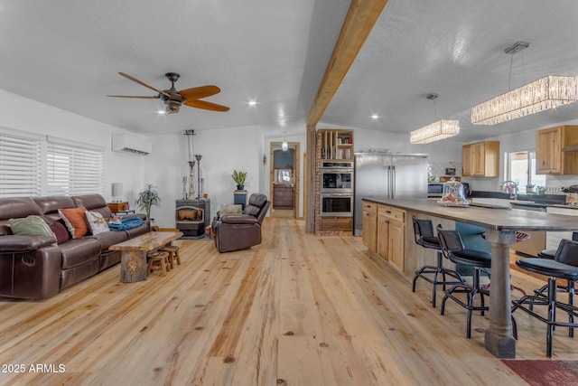 living room with an AC wall unit, lofted ceiling with beams, light hardwood / wood-style flooring, a wood stove, and ceiling fan