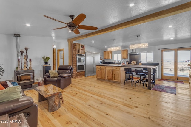 living room featuring light wood-type flooring, vaulted ceiling with beams, ceiling fan, a wood stove, and a textured ceiling