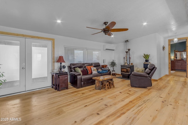 living room with light hardwood / wood-style floors, ceiling fan, french doors, a wall mounted air conditioner, and a wood stove