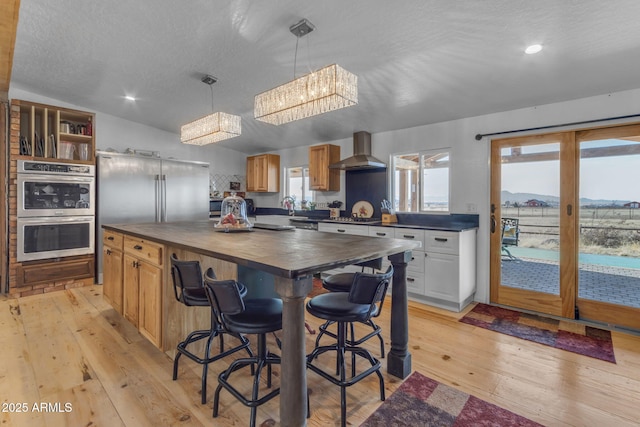 kitchen featuring a chandelier, stainless steel appliances, hanging light fixtures, a kitchen island, and wall chimney range hood