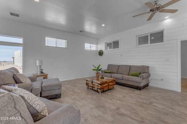 living room with ceiling fan, wooden walls, and light hardwood / wood-style flooring