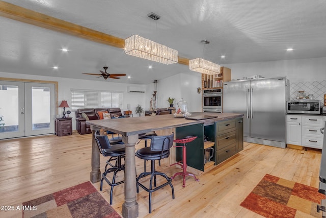 kitchen featuring appliances with stainless steel finishes, hanging light fixtures, a wall mounted AC, white cabinetry, and ceiling fan with notable chandelier