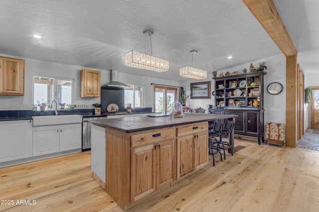 kitchen with hanging light fixtures, a center island, wall chimney exhaust hood, a textured ceiling, and light hardwood / wood-style flooring