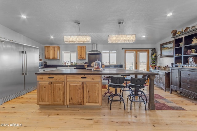 kitchen with light hardwood / wood-style floors, hanging light fixtures, wall chimney range hood, and built in fridge