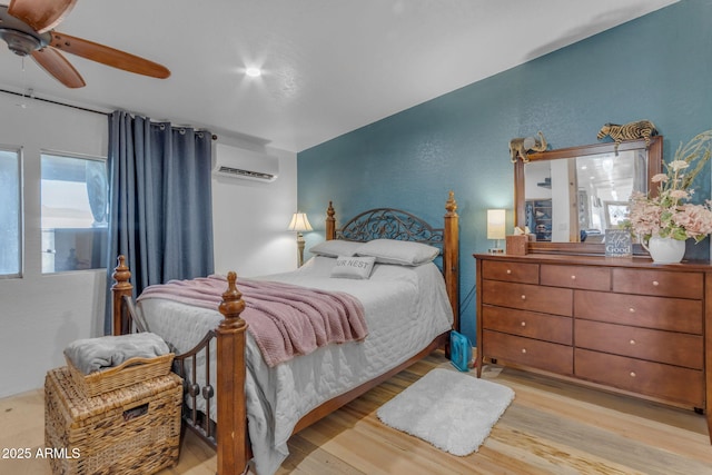 bedroom featuring ceiling fan, light wood-type flooring, and a wall unit AC