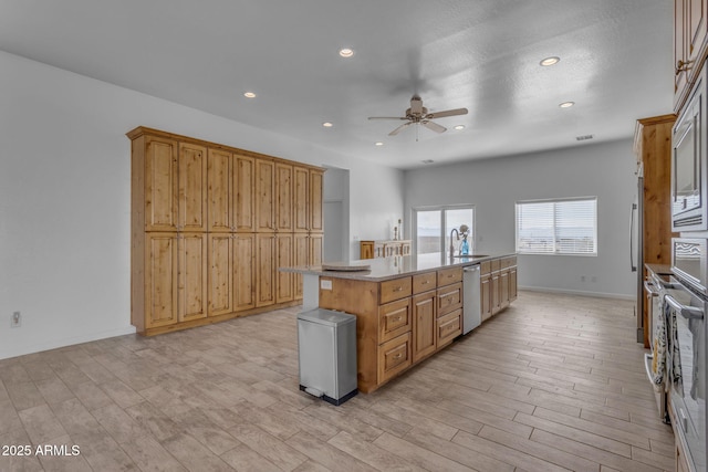 kitchen with sink, ceiling fan, light hardwood / wood-style flooring, a center island with sink, and appliances with stainless steel finishes