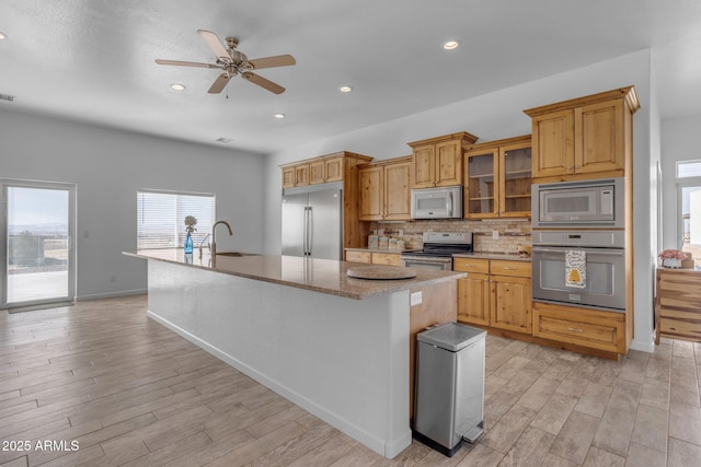 kitchen with built in appliances, light wood-type flooring, a kitchen island with sink, and sink