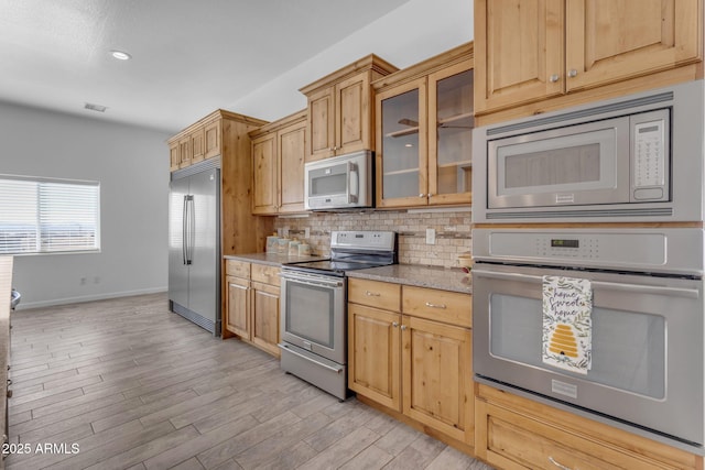 kitchen featuring built in appliances, backsplash, light hardwood / wood-style floors, and light stone countertops