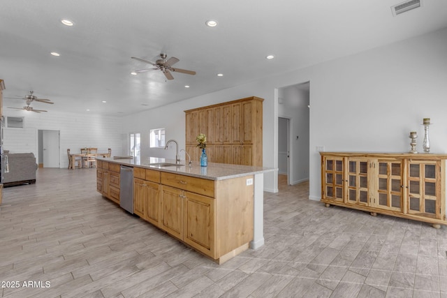 kitchen with dishwasher, an island with sink, light stone countertops, ceiling fan, and sink