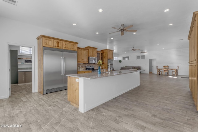 kitchen featuring stainless steel appliances, light stone counters, ceiling fan, light wood-type flooring, and a center island with sink