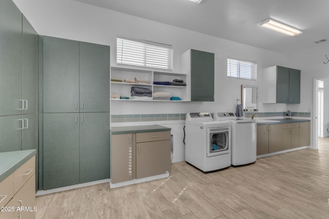 clothes washing area with sink, washing machine and dryer, light wood-type flooring, and cabinets