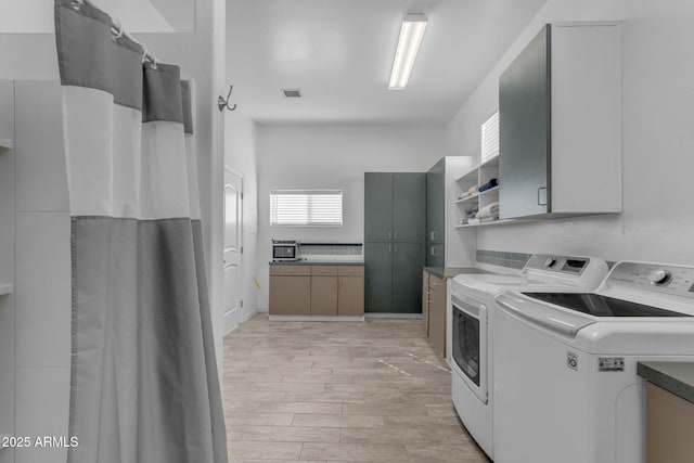 laundry area featuring separate washer and dryer, cabinets, and light hardwood / wood-style floors