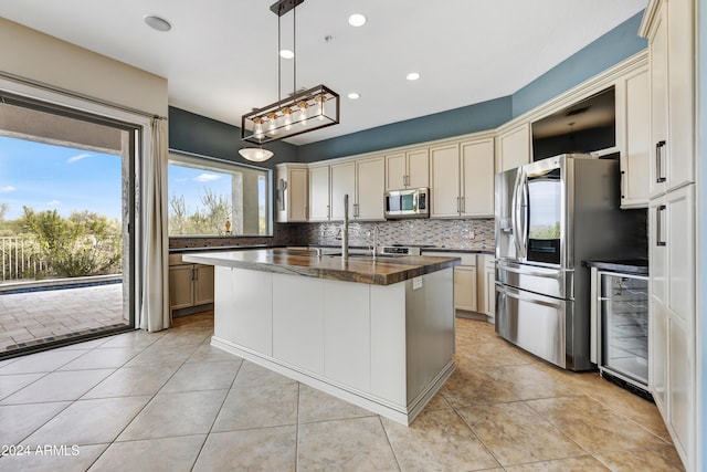 kitchen featuring decorative light fixtures, stainless steel appliances, light tile patterned floors, and an island with sink