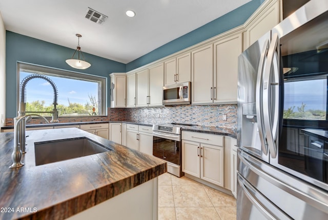 kitchen with backsplash, hanging light fixtures, sink, appliances with stainless steel finishes, and butcher block countertops