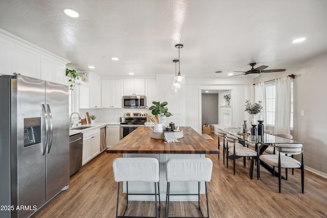 kitchen featuring appliances with stainless steel finishes, white cabinetry, a kitchen island, a sink, and butcher block countertops