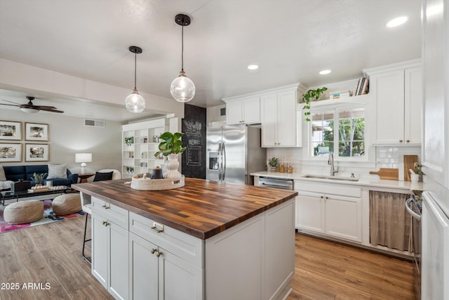 kitchen with stainless steel appliances, a sink, wood counters, open floor plan, and backsplash