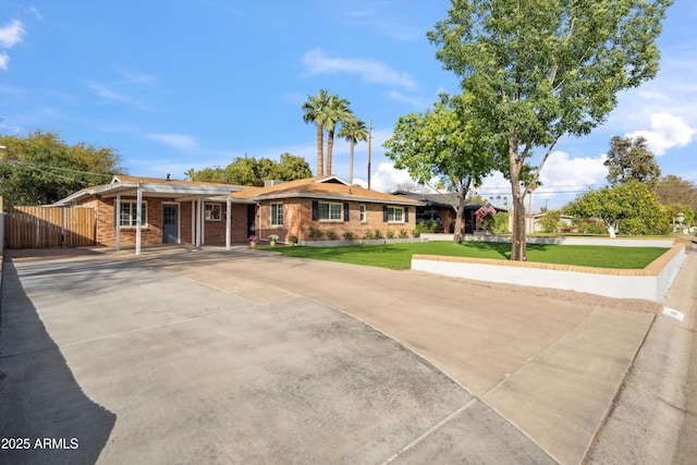 ranch-style home featuring a front yard, concrete driveway, brick siding, and fence