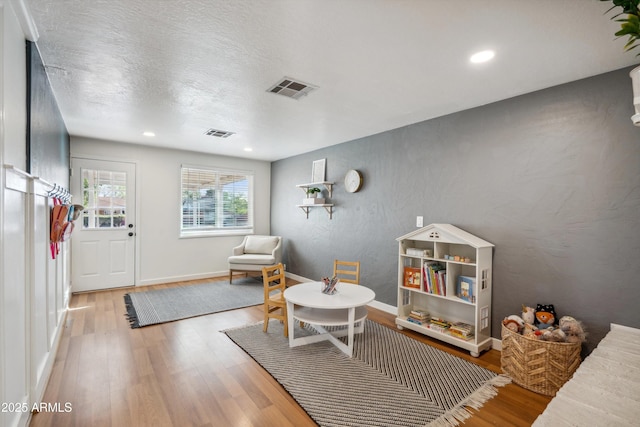 rec room featuring a textured ceiling, a textured wall, wood finished floors, visible vents, and baseboards