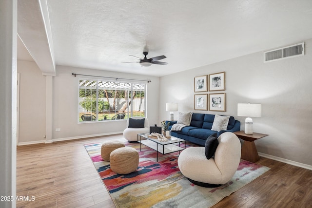 living area with a ceiling fan, visible vents, baseboards, and wood finished floors