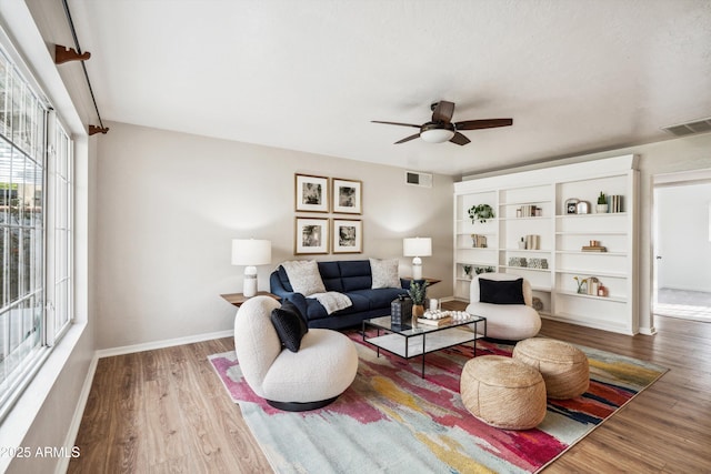 living area with a ceiling fan, visible vents, baseboards, and wood finished floors