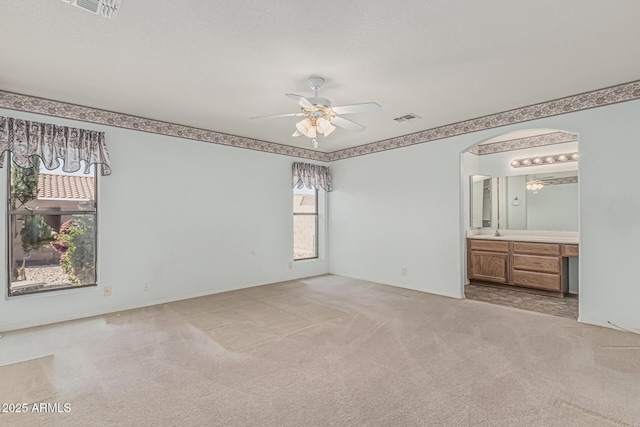 unfurnished bedroom with carpet flooring, arched walkways, visible vents, and a sink