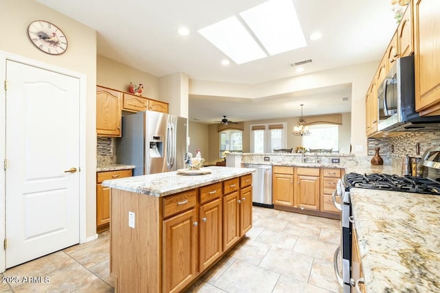 kitchen featuring light stone counters, a skylight, appliances with stainless steel finishes, a kitchen island, and a peninsula