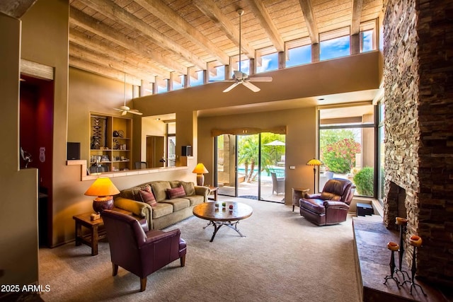 carpeted living area with wood ceiling, a ceiling fan, a fireplace, beamed ceiling, and a high ceiling