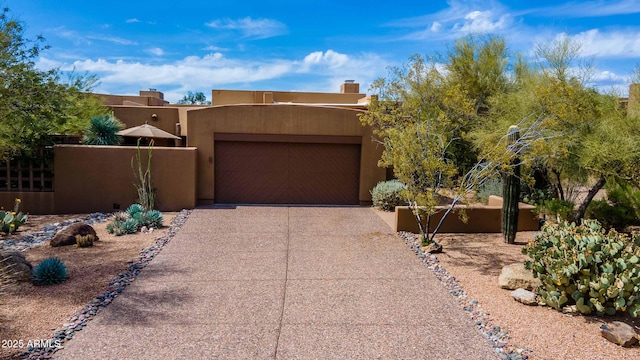 pueblo-style house with fence, stucco siding, a chimney, an attached garage, and driveway