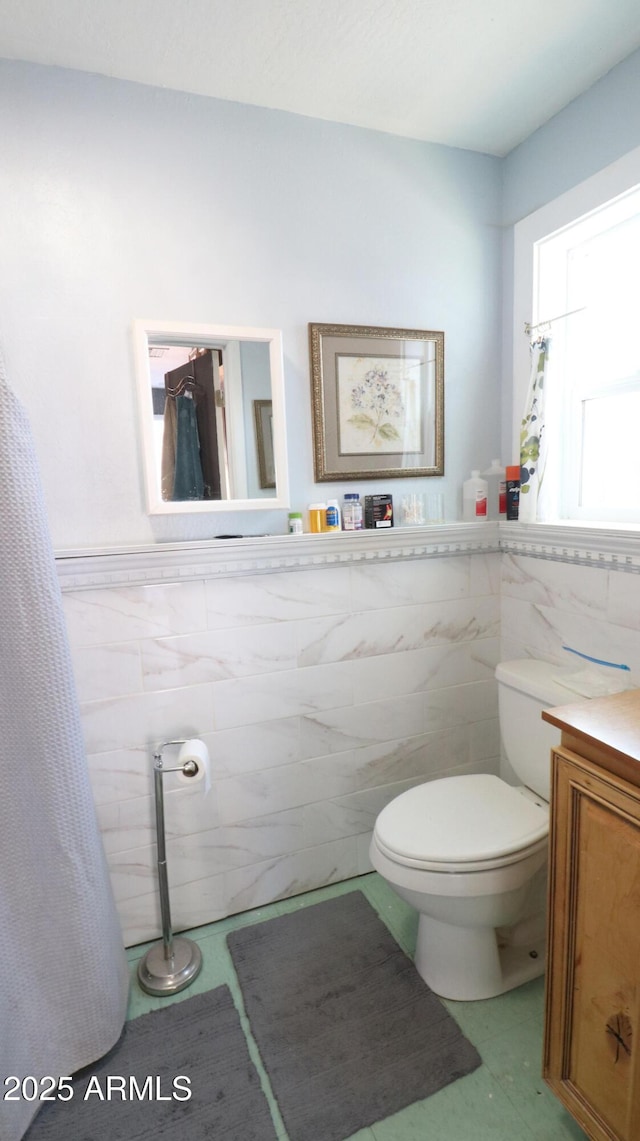 bathroom featuring a wainscoted wall, tile walls, toilet, and vanity