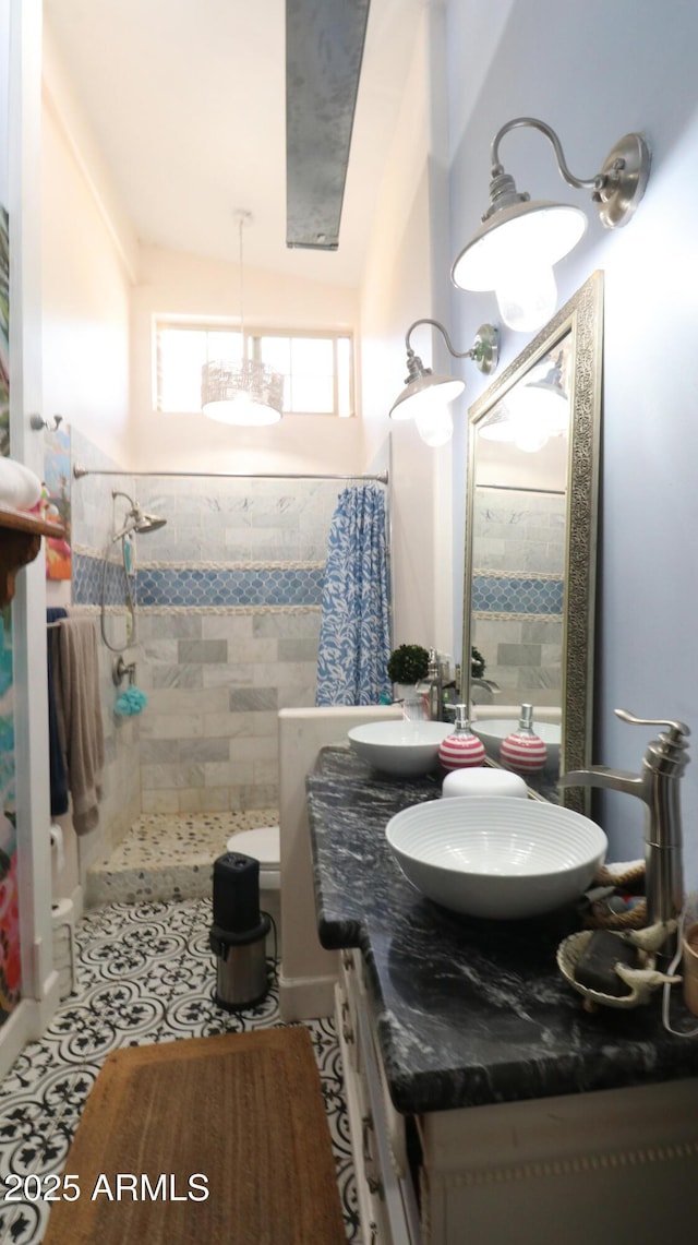 bathroom with a sink, double vanity, a tile shower, and tile patterned floors