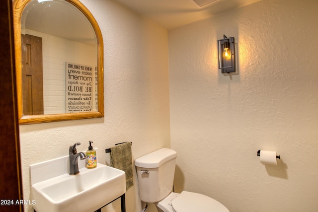 half bathroom featuring toilet, a textured wall, and a sink