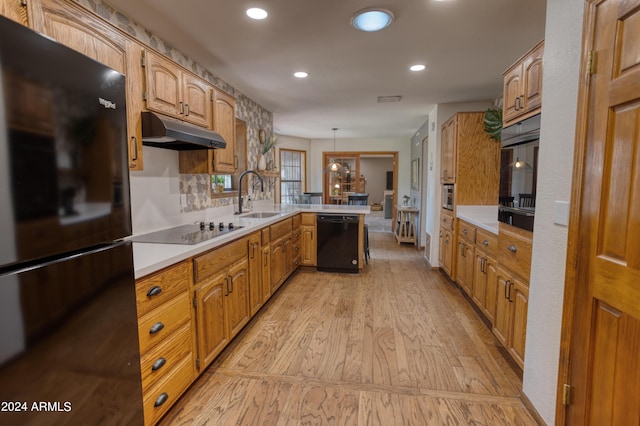 kitchen featuring a sink, black appliances, light wood-type flooring, a peninsula, and under cabinet range hood