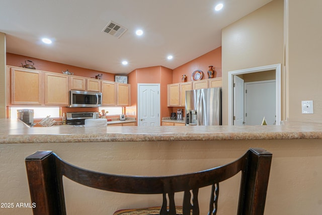 kitchen featuring lofted ceiling, light brown cabinets, stainless steel appliances, a peninsula, and visible vents