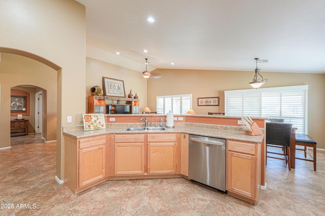 kitchen featuring arched walkways, dishwasher, vaulted ceiling, light brown cabinetry, and a sink