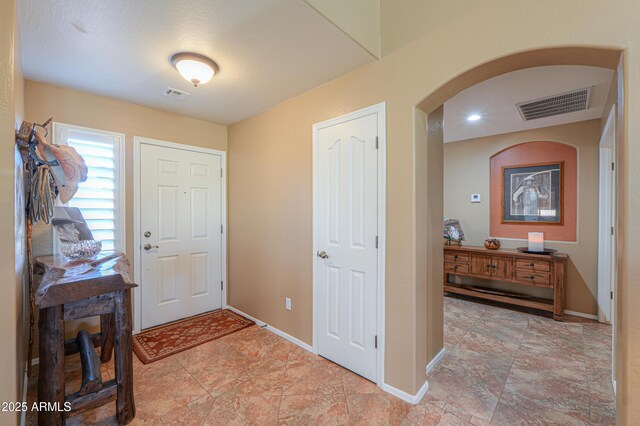 foyer entrance featuring arched walkways, visible vents, and baseboards