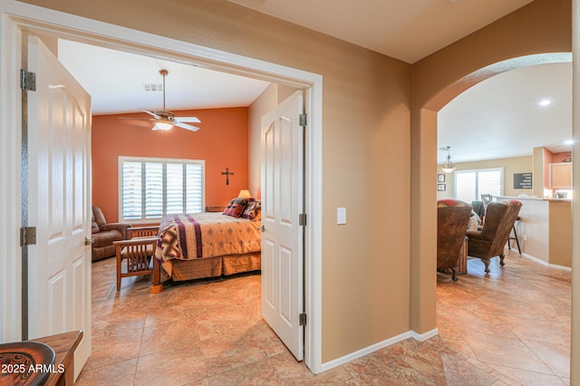 bedroom with arched walkways, lofted ceiling, visible vents, stone finish floor, and baseboards