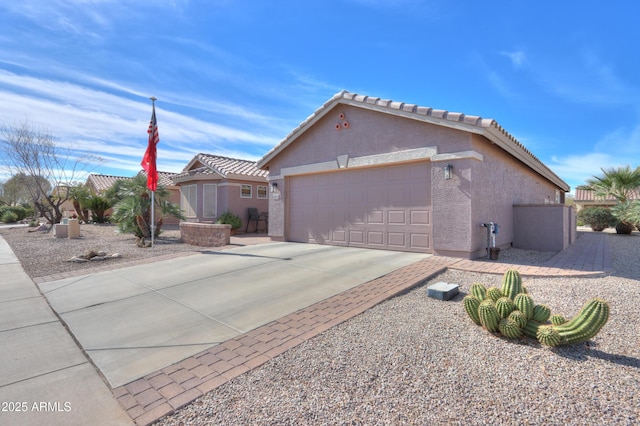 view of side of home featuring concrete driveway, a tiled roof, an attached garage, and stucco siding