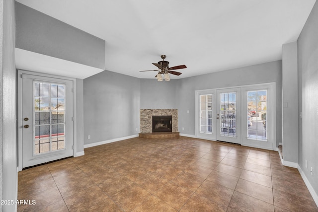 unfurnished living room featuring tile patterned floors, a fireplace with raised hearth, baseboards, and a ceiling fan