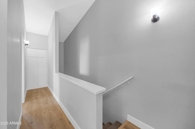 hall with an upstairs landing, baseboards, and wood finished floors
