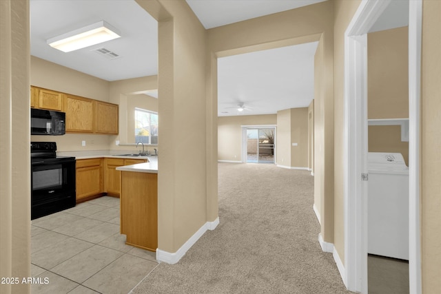 kitchen featuring light brown cabinetry, sink, light colored carpet, washer / clothes dryer, and black appliances