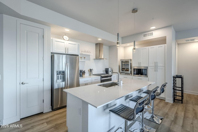 kitchen featuring wall chimney exhaust hood, sink, hanging light fixtures, stainless steel appliances, and white cabinets