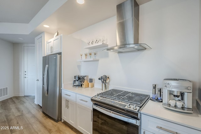 kitchen featuring white cabinetry, appliances with stainless steel finishes, light hardwood / wood-style flooring, and wall chimney range hood