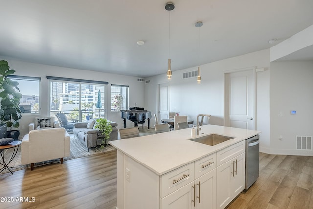 kitchen with sink, white cabinetry, hanging light fixtures, a center island with sink, and stainless steel dishwasher