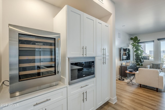 kitchen with white cabinetry, light hardwood / wood-style floors, beverage cooler, and black microwave