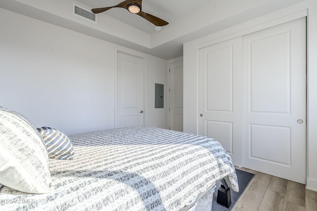 bedroom with wood-type flooring, electric panel, a closet, and ceiling fan