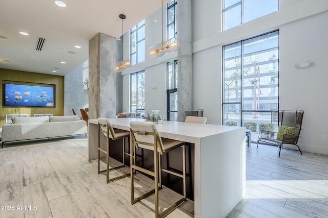 interior space featuring a towering ceiling, hanging light fixtures, light hardwood / wood-style floors, and a breakfast bar area