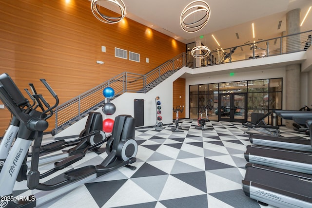 exercise room featuring french doors, a high ceiling, and wood walls