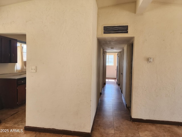 hall with dark tile patterned floors, visible vents, and a textured wall