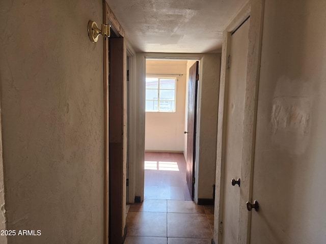 corridor with light tile patterned flooring, a textured wall, and a textured ceiling