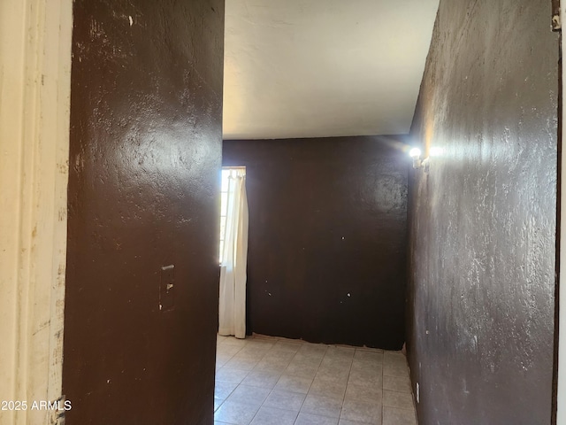 corridor featuring light tile patterned floors and a textured wall